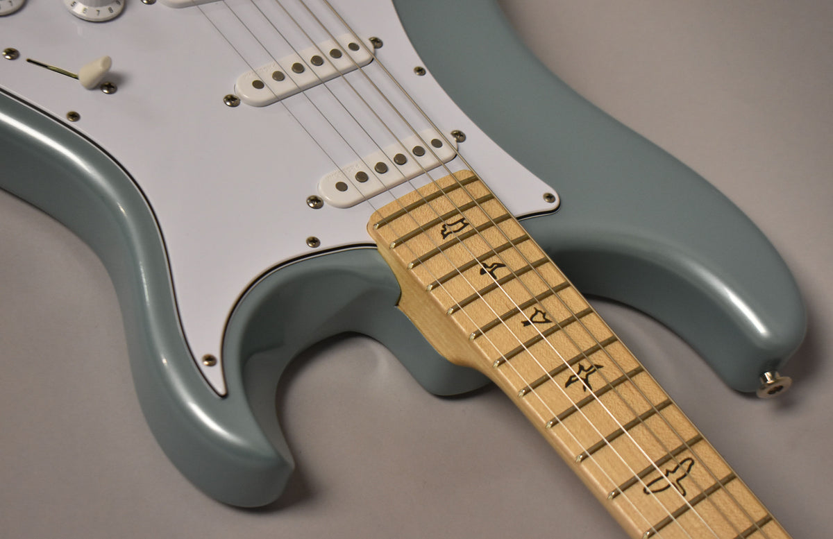 Close-up of the guitar's Polar Blue body and white pickguard, with the light maple fretboard and bird inlays angled across the foreground.