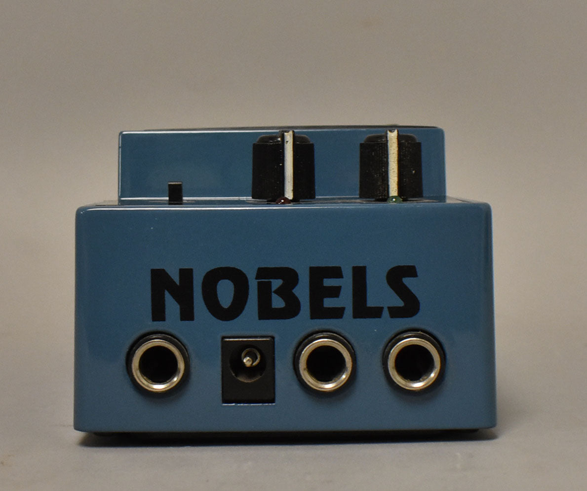 Front of the blue Nobels pedal, showing three jacks, a power input and two black knobs on top.