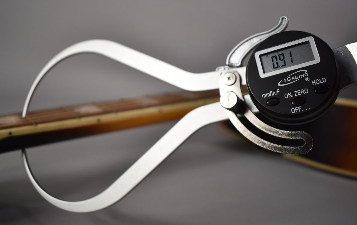 A digital caliper measures the guitar's aged sunburst neck, showing "0.91" on its display.