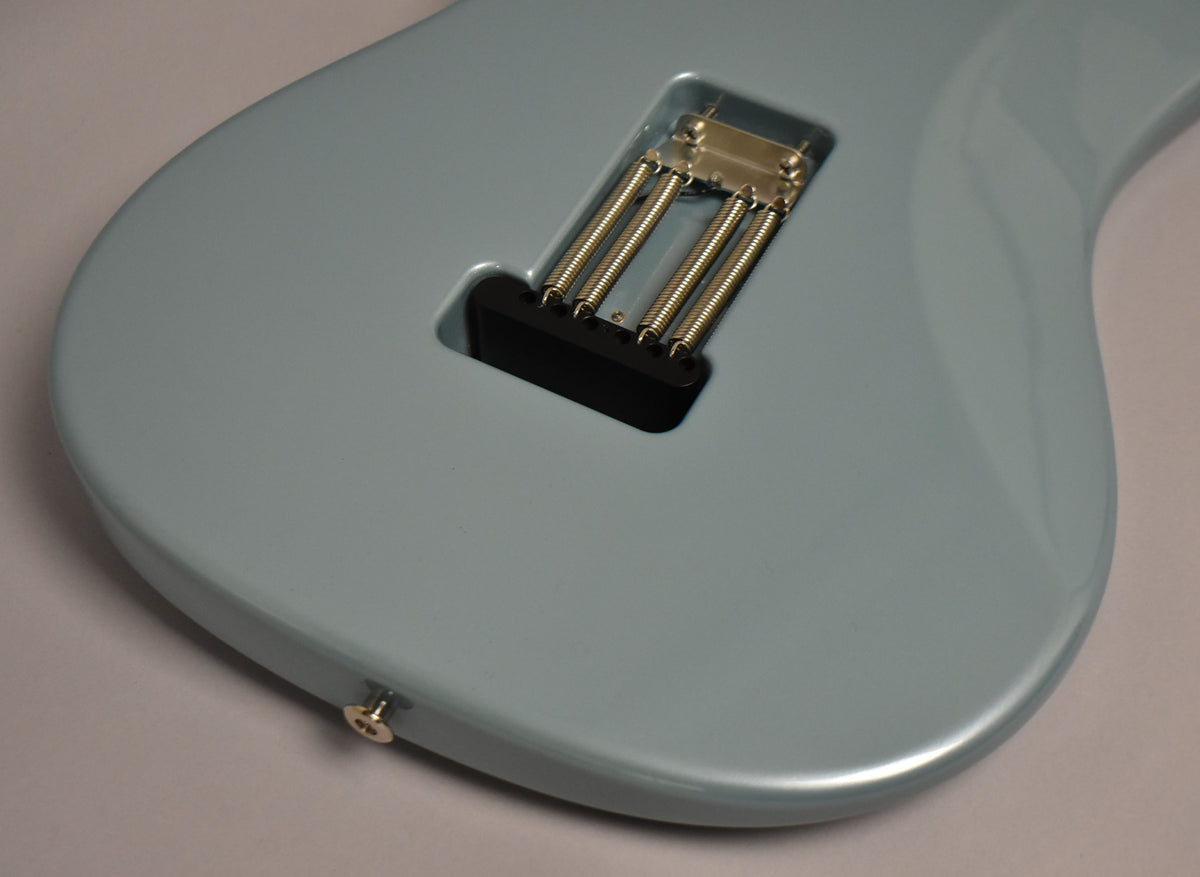 The back of a light blue electric guitar, showing the tremolo spring cavity with four springs and a chrome output jack.