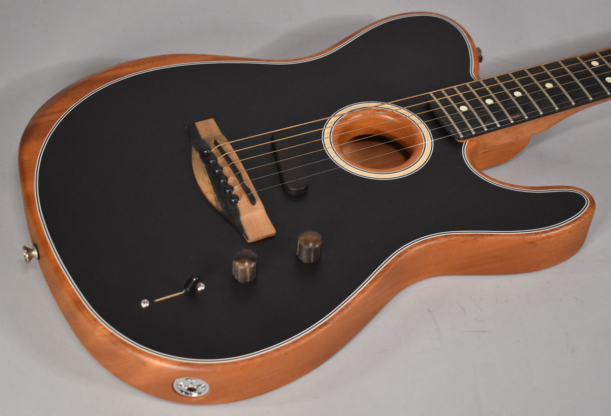 The black matte Telecaster-style guitar body with natural wood sides is angled from the upper right, showing the bridge, soundhole, and controls.