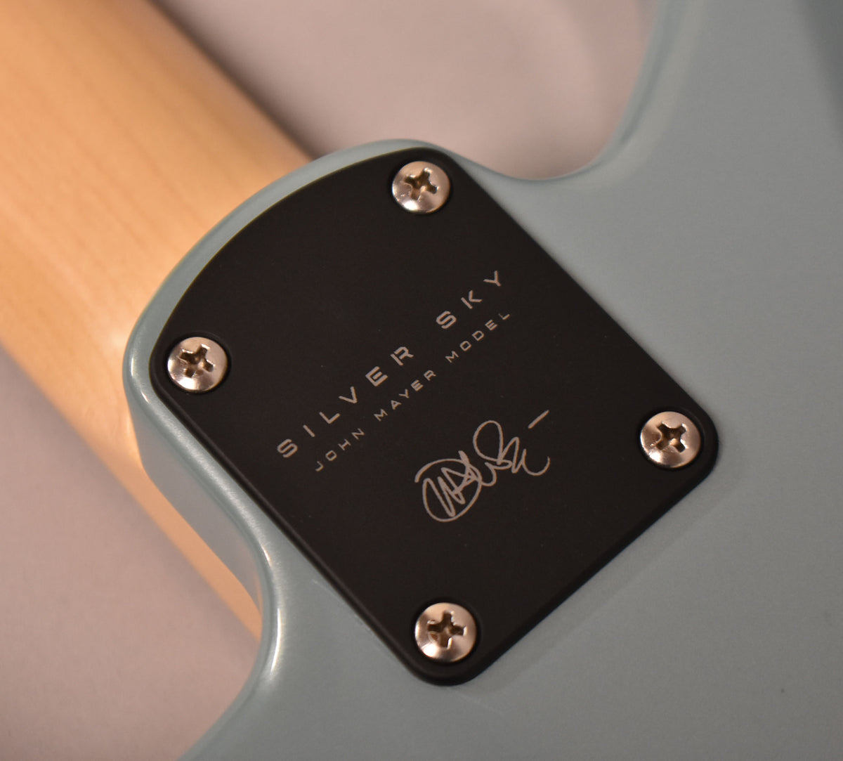 Close-up of the guitar's neck plate, a black rectangle with "SILVER SKY JOHN MAYER MODEL" and a signature, screwed into the light blue body.