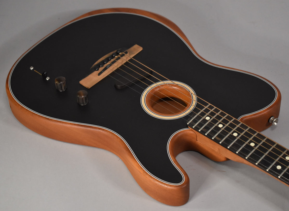 The black matte-finish Acoustasonic Telecaster body, with natural wood sides and binding, is angled from the upper left, showing the soundhole, bridge, and two control knobs.