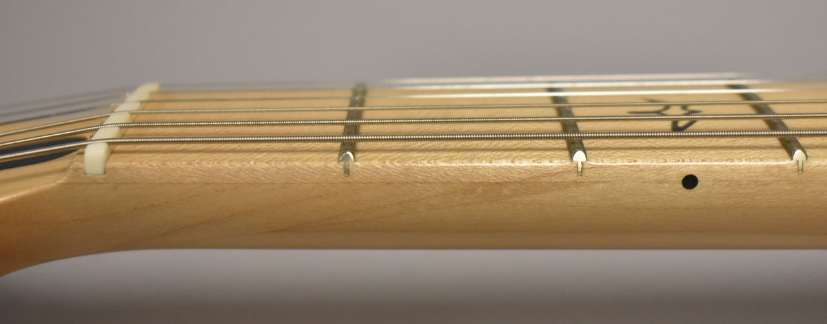 Close-up of the light maple fretboard and frets, with a white nut and six strings, and a black dot side marker.