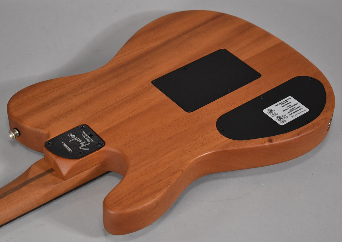 The back of a light brown wooden guitar body, showing two black control plates and the neck joint.
