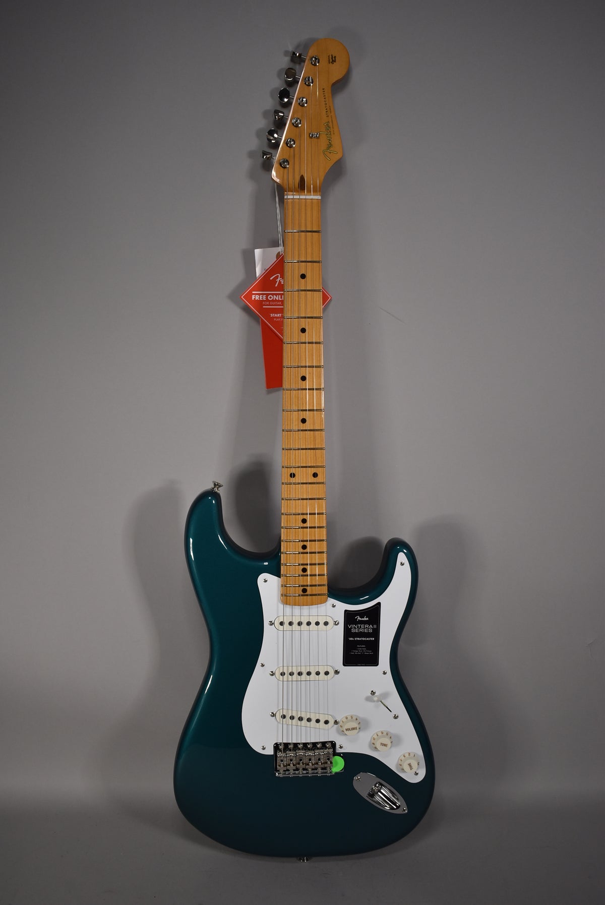 Full-length view of a glossy ocean turquoise Stratocaster with a maple neck, white pickguard, three single-coil pickups, and chrome hardware.