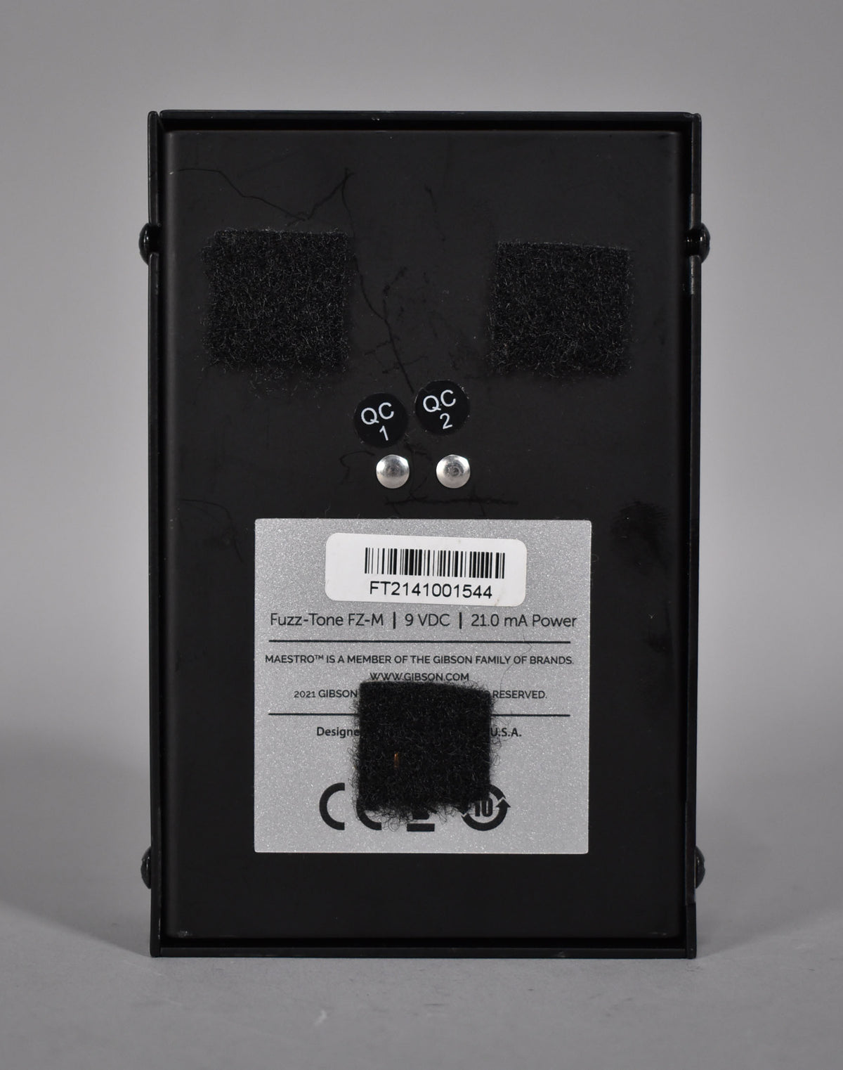 The black pedal's underside is visible, showing a silver information sticker, two QC stickers, and three patches of black hook-and-loop tape.