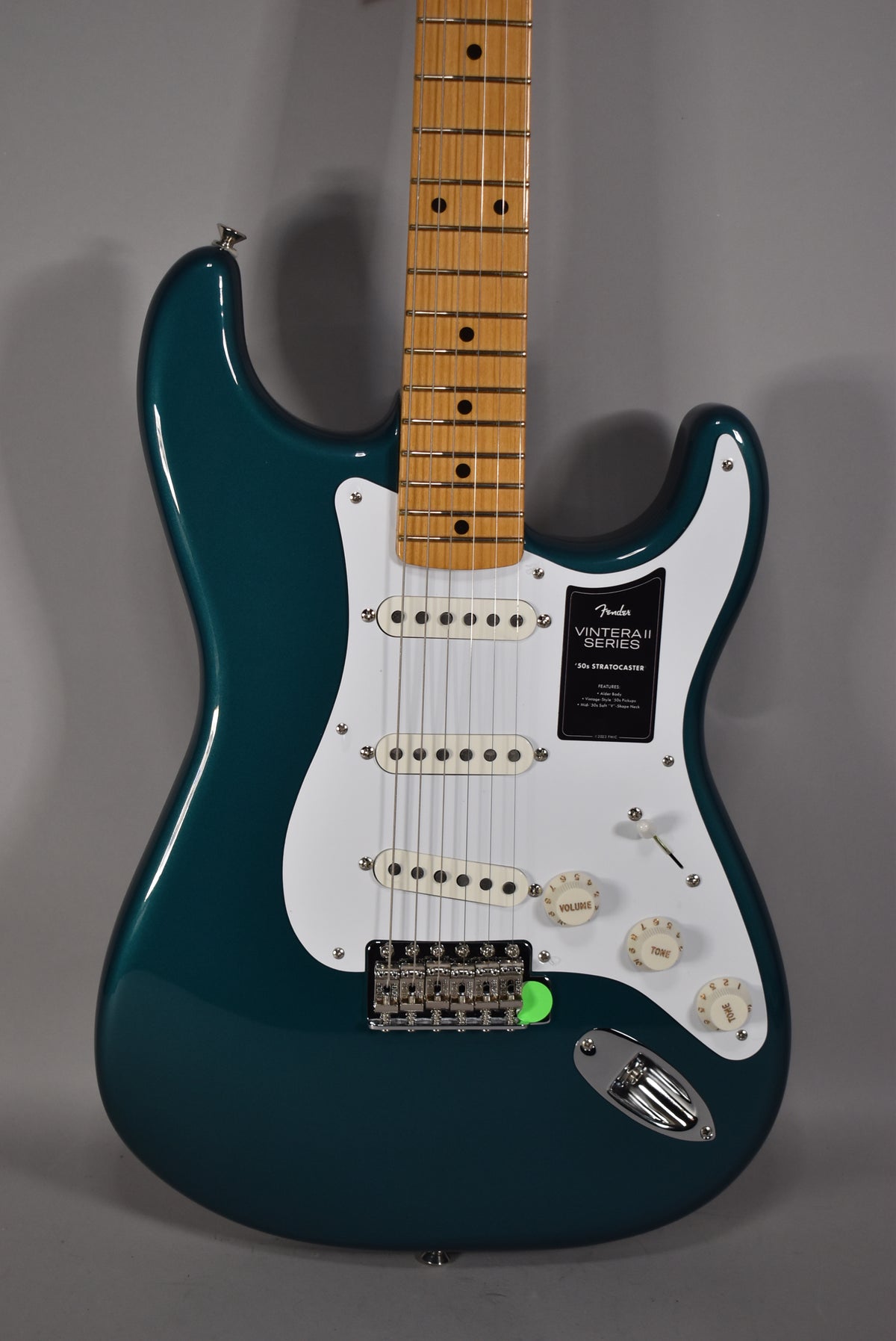 A full-frame, eye-level shot of a glossy ocean turquoise Stratocaster with a white pickguard, three single-coil pickups, and a maple neck.