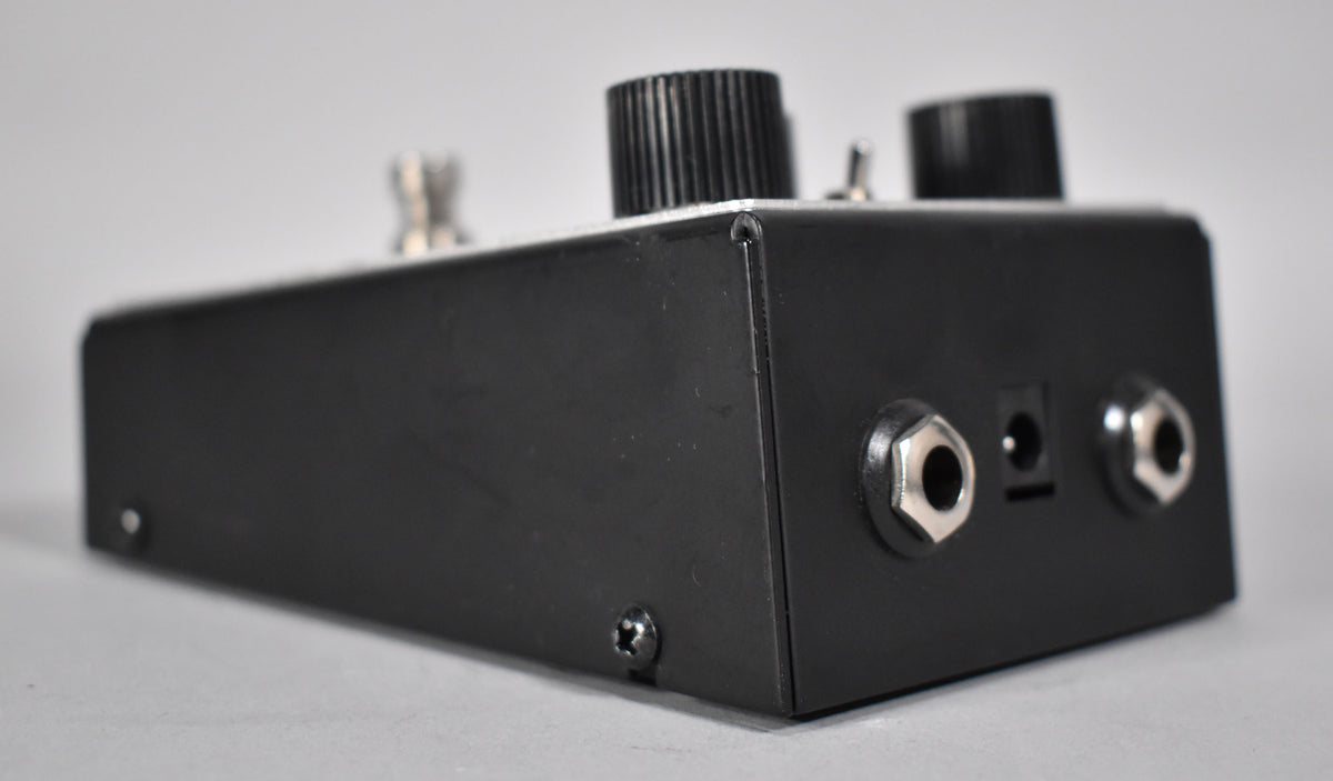 The black pedal is viewed from the right side, showing two silver input jacks and a power input on the back panel.