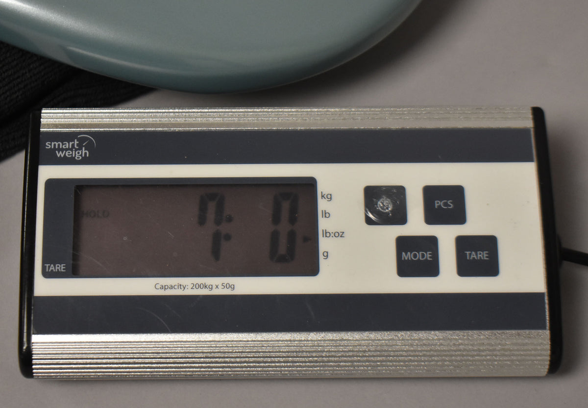 A close-up of a digital scale displaying "7.0" lbs, with a light blue guitar body partially visible at the top.