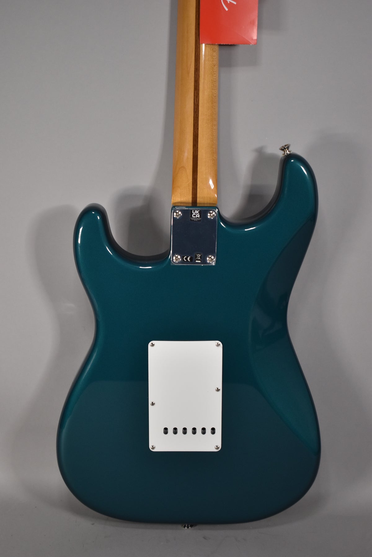 The guitar's back is shown, featuring a glossy ocean turquoise finish, a light wood neck, and a white tremolo cover.
