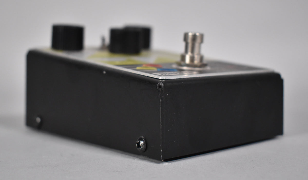 The black pedal is viewed from the right side, showing a silver footswitch and two black knobs on the top, with some paint chips.