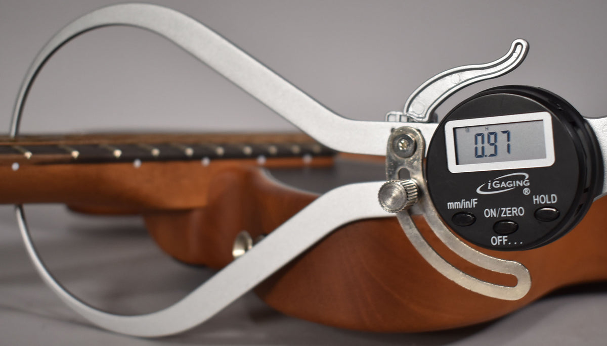 A digital caliper measures the neck thickness at the heel of the black Acoustasonic Telecaster, displaying 0.97.