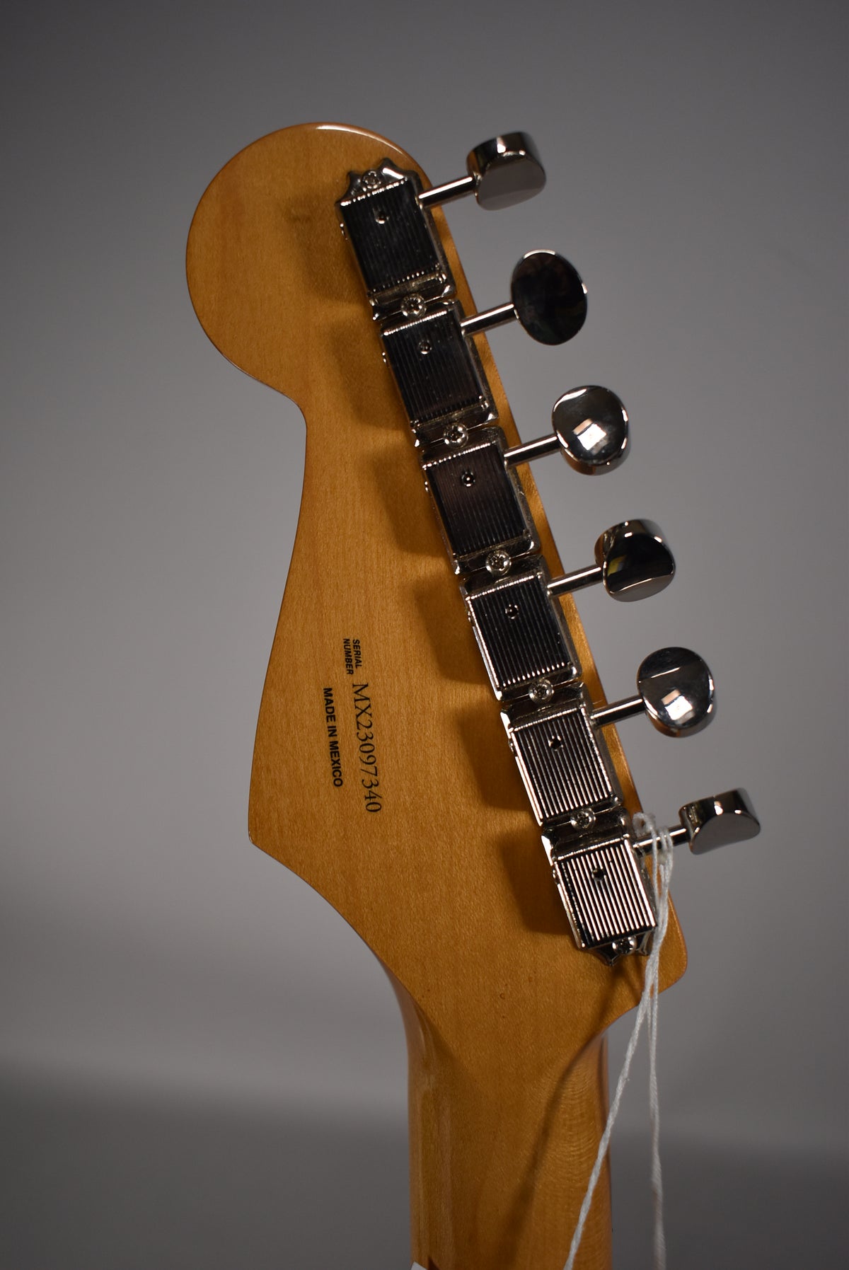The back of the guitar's headstock and top of the neck, showing six chrome tuning machines and the serial number on the wood.
