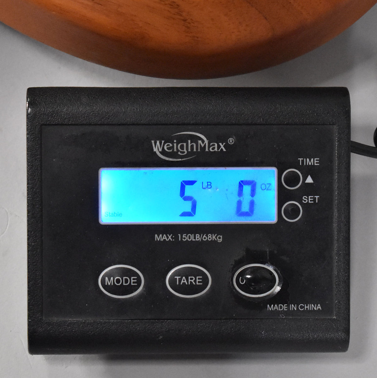 The guitar's weight is displayed as 5 lbs 0 oz on a black digital scale, with a portion of its brown wooden body visible above.