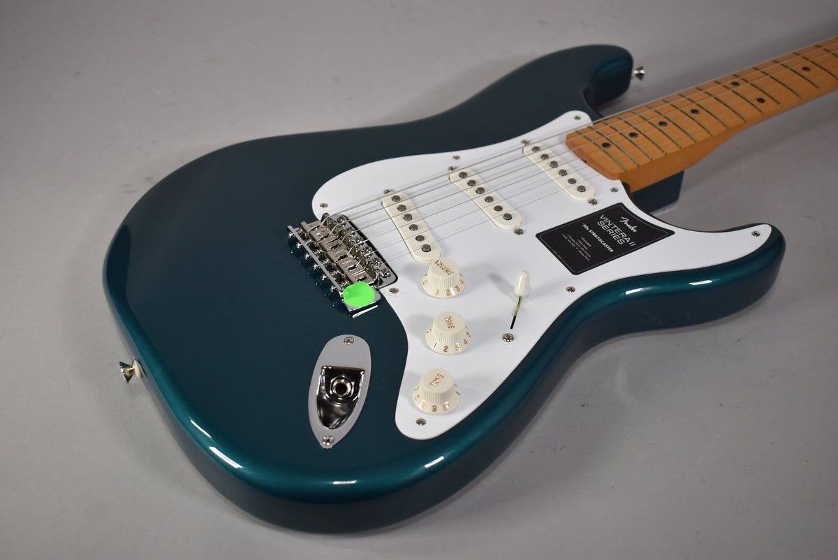 The glossy Ocean Turquoise Stratocaster is angled from the lower right, showing its white pickguard, three cream pickups, and maple neck.