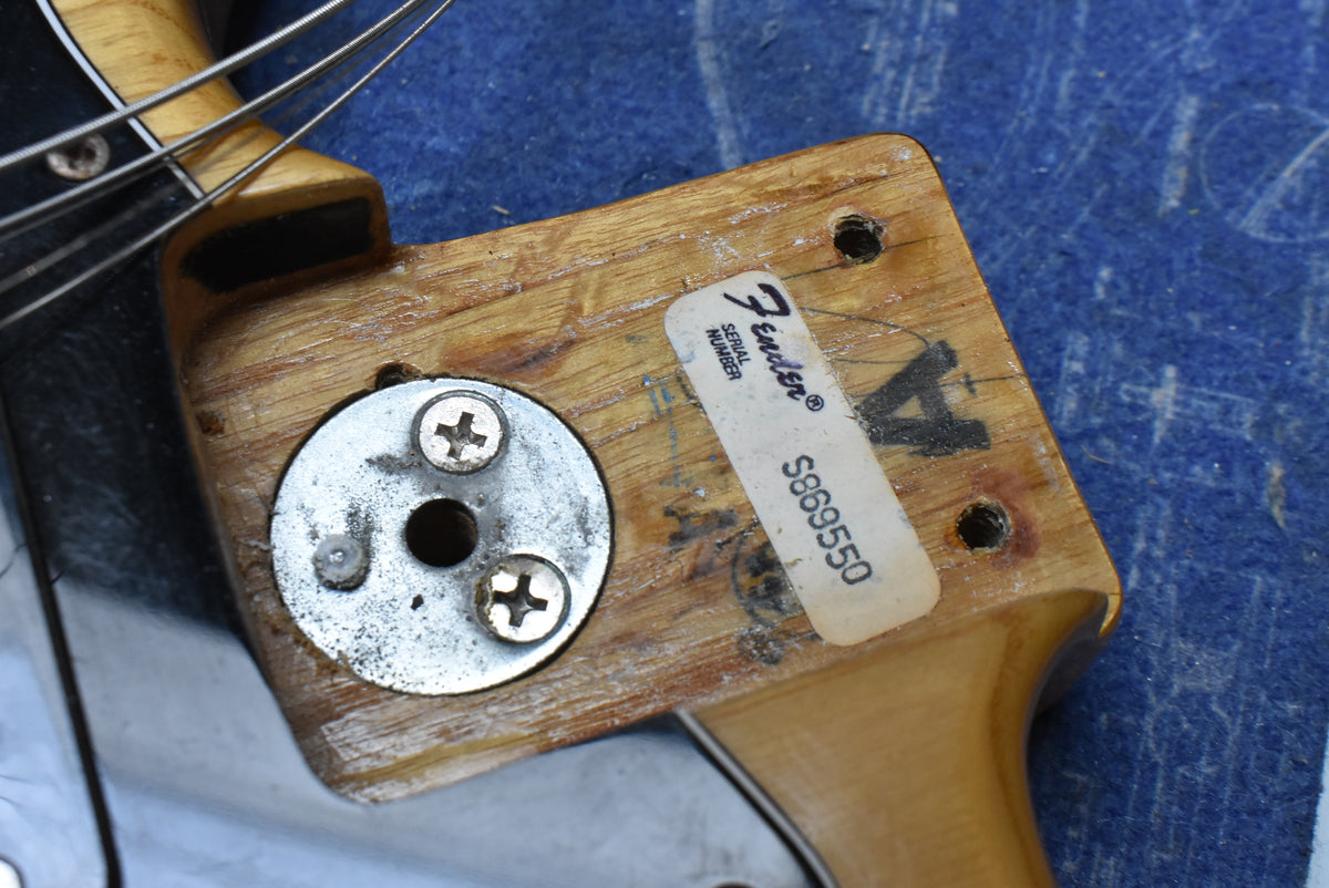 Close-up of the natural wood neck heel and body joint, showing the serial number sticker and a circular metal plate with three screws.