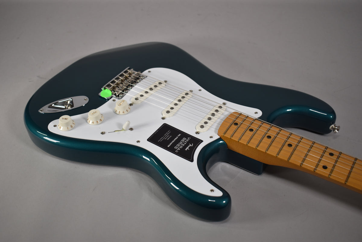 The Ocean Turquoise Stratocaster body is angled from the upper left, showing the white pickguard, three single-coil pickups, and maple neck.