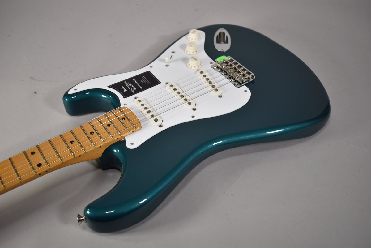 The Ocean Turquoise Stratocaster is angled right, showing its glossy body, white pickguard, three single-coil pickups, and maple fretboard.
