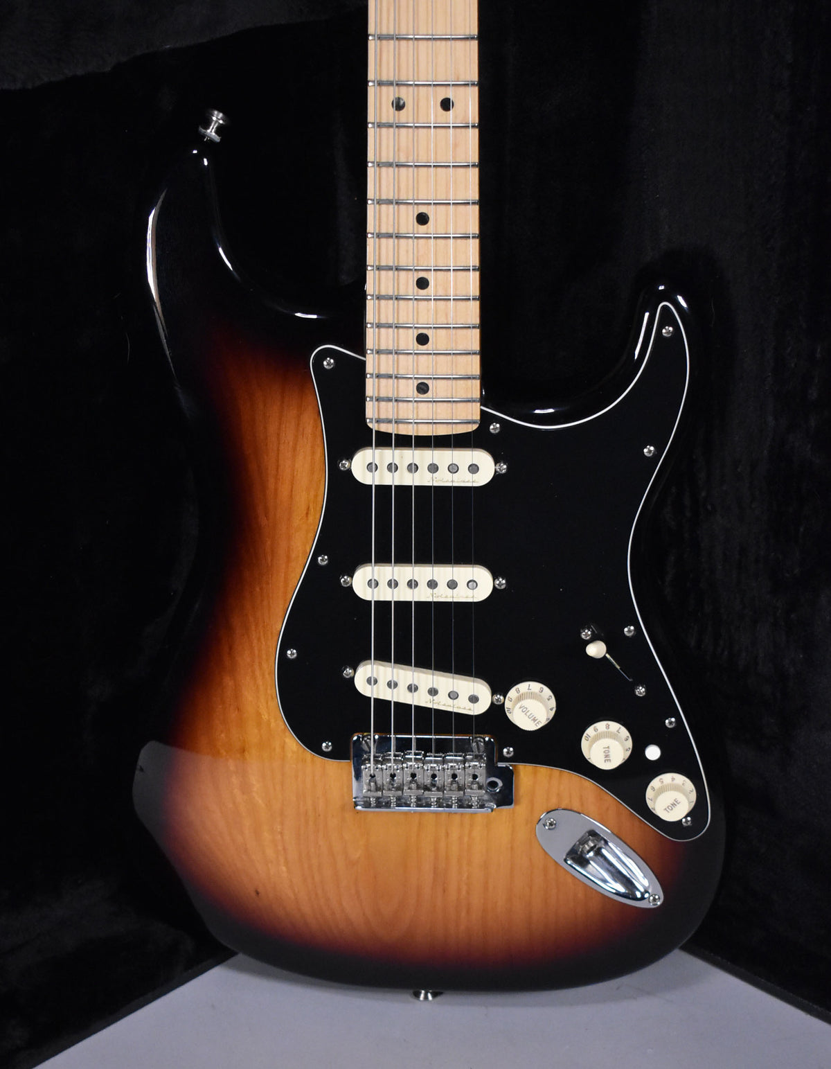Full-frame, glossy 3-tone sunburst electric guitar with a black pickguard, three cream single-coil pickups, and a maple fretboard.