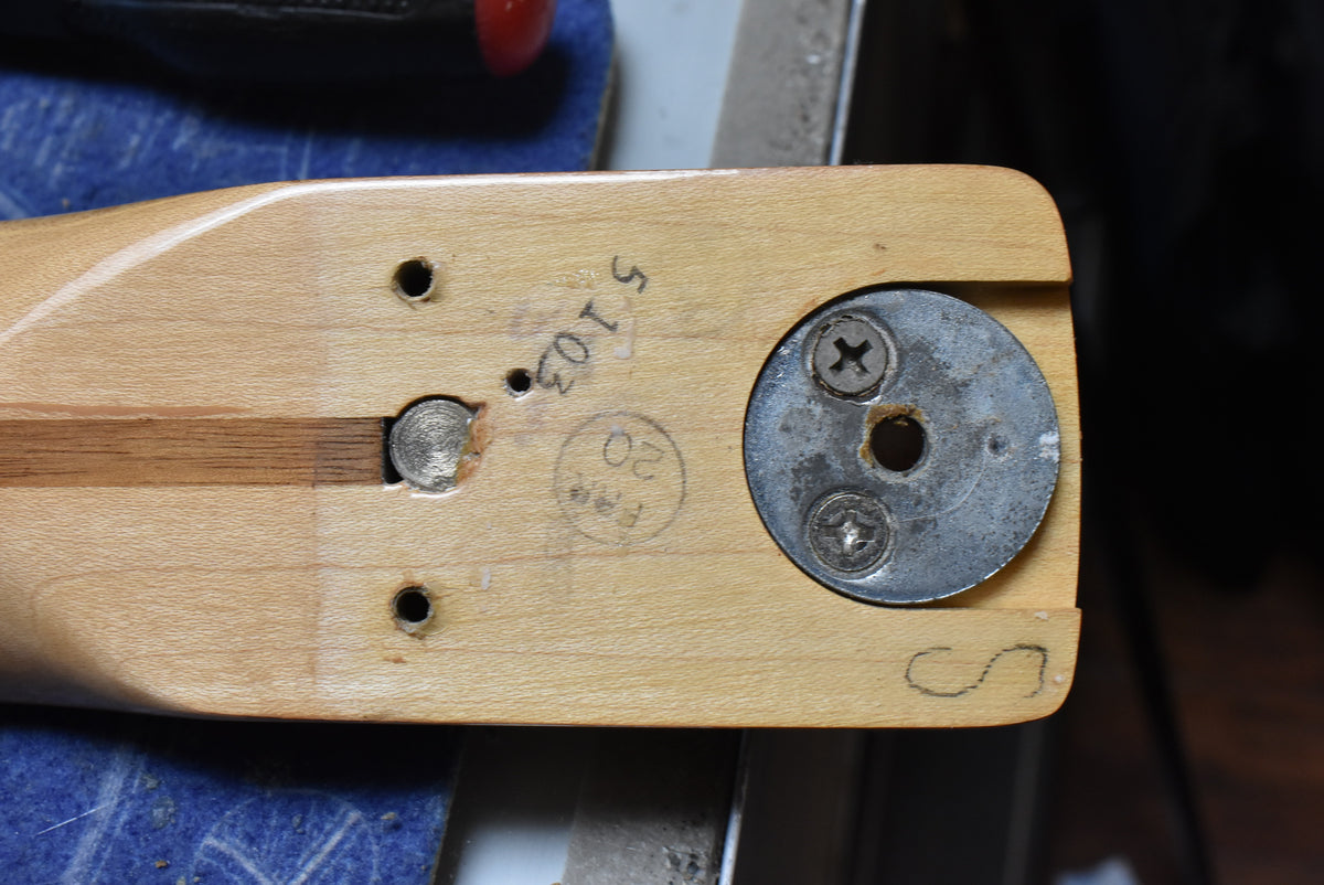 Close-up of the natural finish neck heel with a metal disc, two screw holes, and a visible truss rod adjustment.