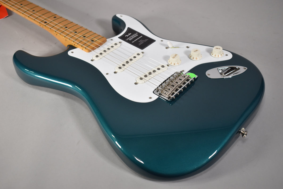 The glossy Ocean Turquoise Stratocaster body is angled from the lower left, showing the white pickguard, three single-coil pickups, and chrome hardware.