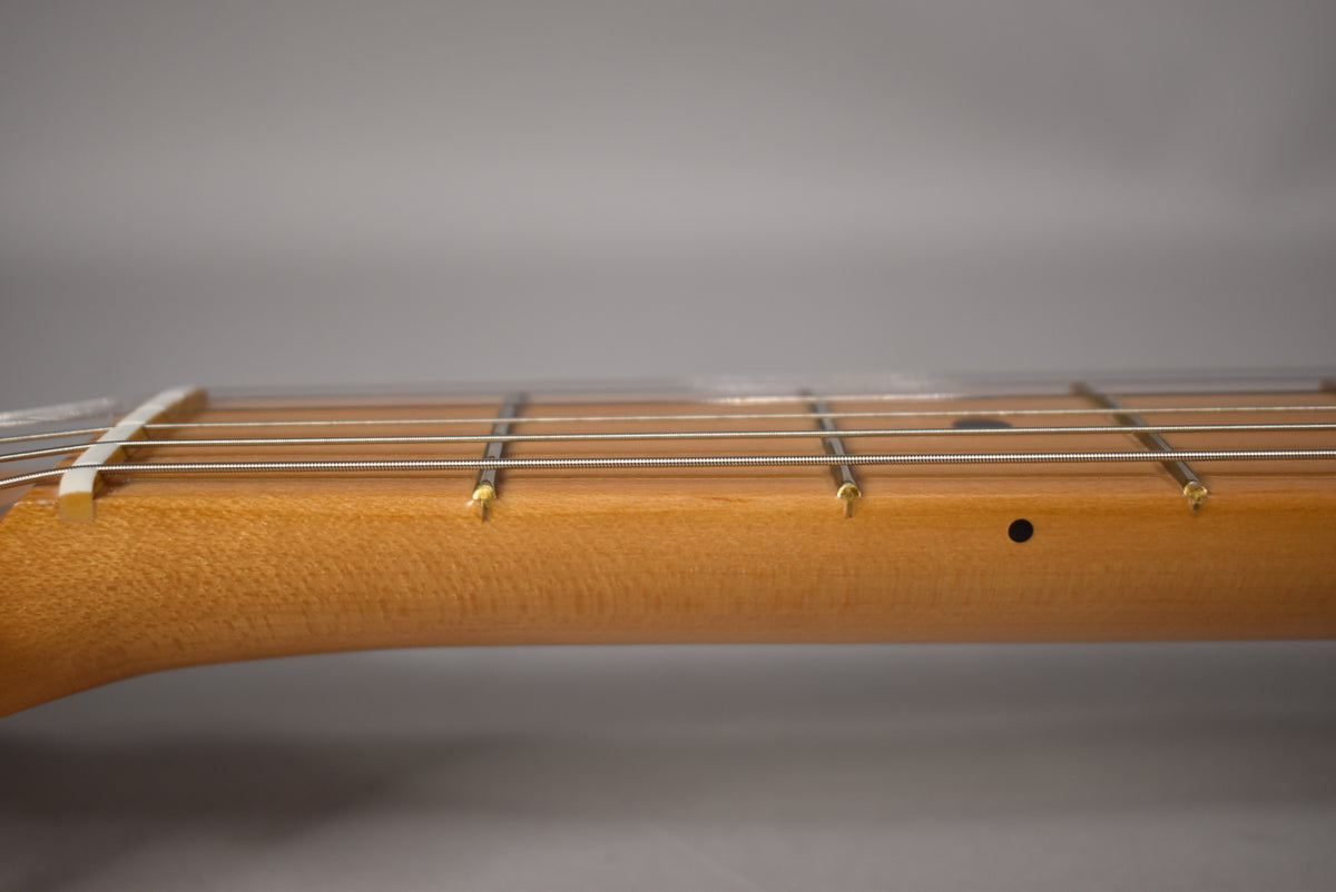 Close-up of the light brown maple neck and fretboard, showing the first few frets, strings, and a black dot inlay.