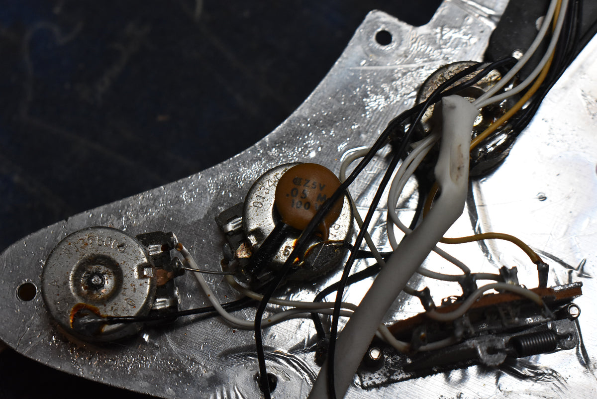 Close-up of the guitar's internal wiring, showing two silver potentiometers, a brown capacitor, and a bundle of black, white, and yellow wires.