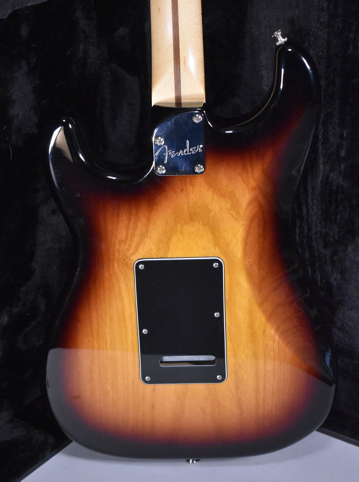 The guitar's back, in 3-tone sunburst, shows a chrome neck plate, a black tremolo cover, and a maple neck with a dark stripe.