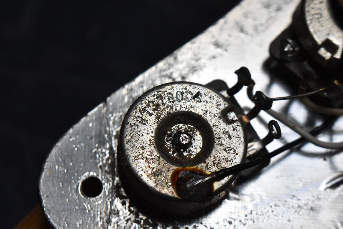 Close-up of a tarnished metal potentiometer with soldered wires, showing the number "13778004" and "R" stamped on its surface.