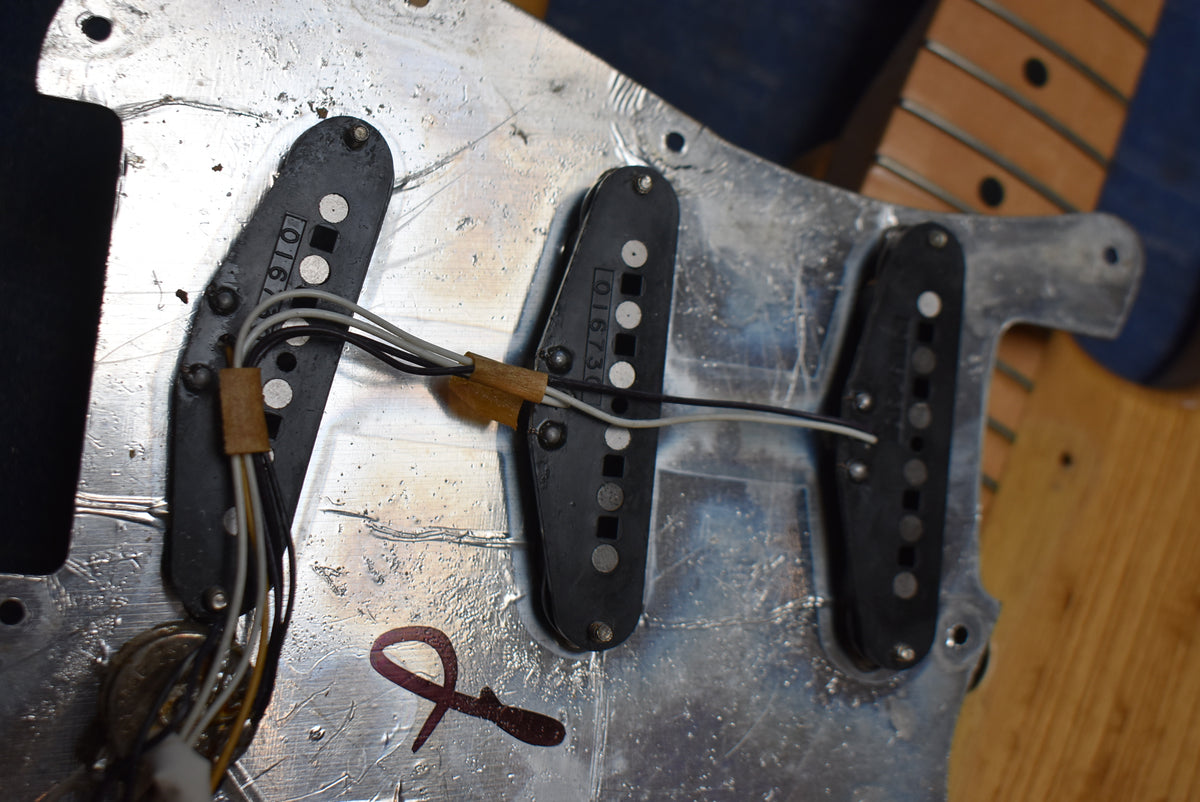 Close-up of three black single-coil pickups and wiring on a scratched aluminum pickguard, with a maple neck visible at the right.