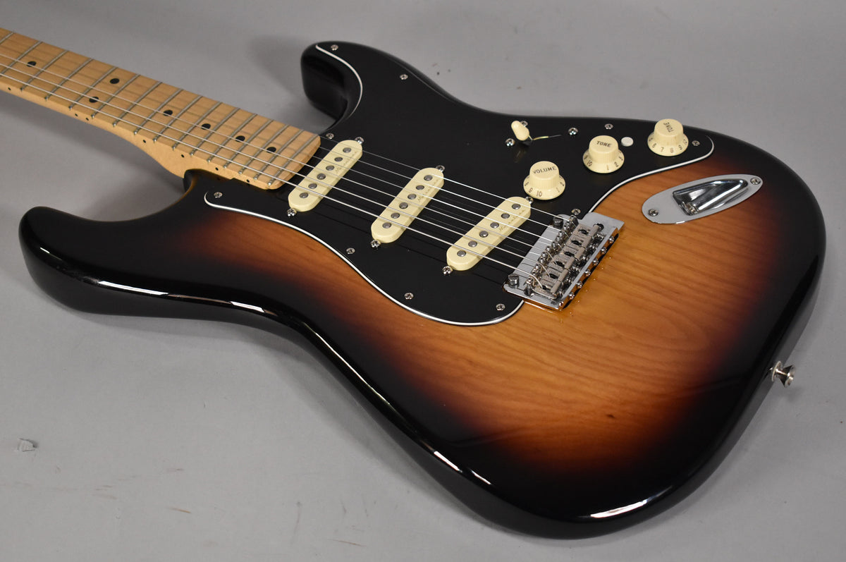 A 3-tone sunburst electric guitar, angled from the neck, shows a black pickguard, three cream single-coil pickups, and chrome hardware.
