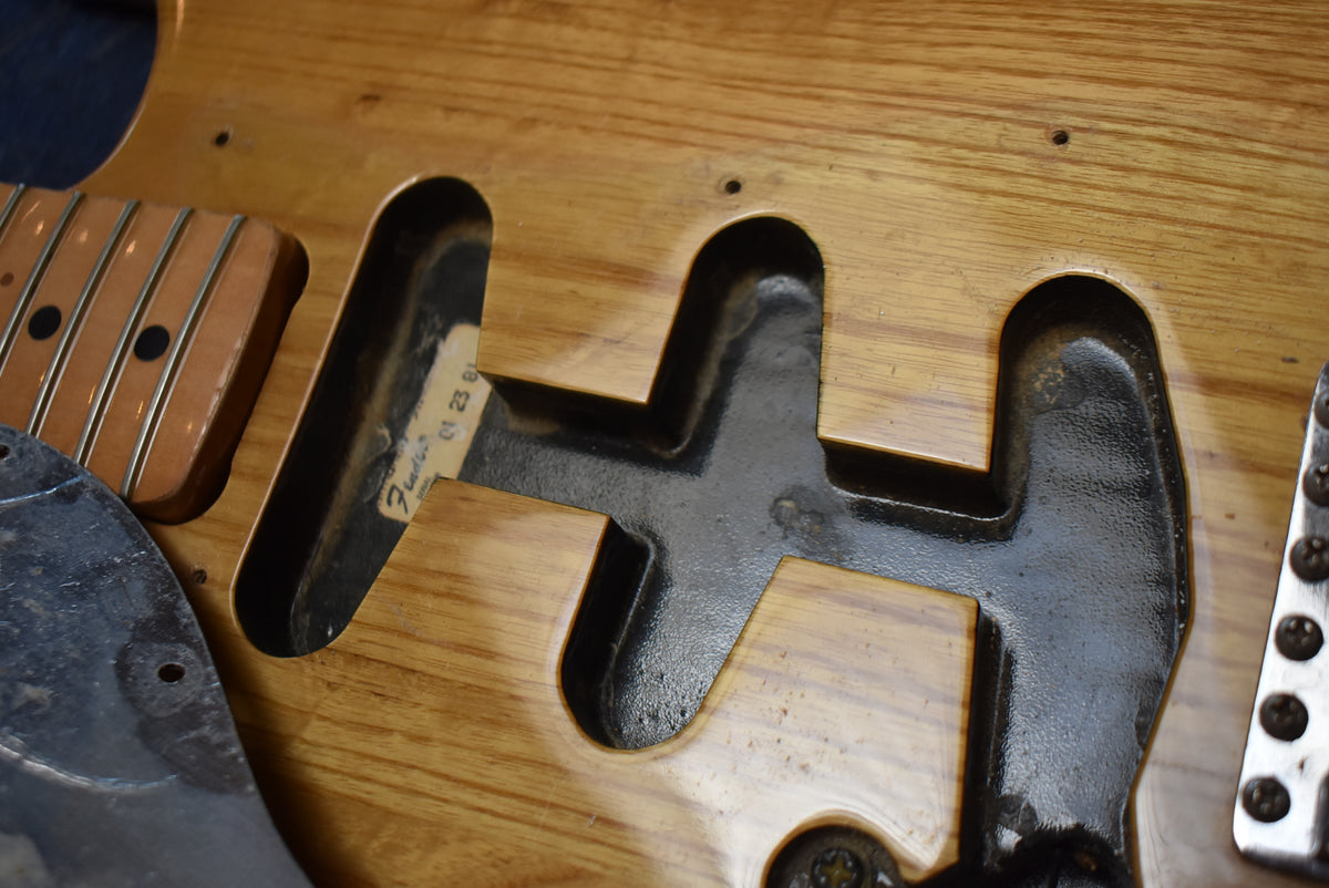 Close-up of the natural wood body's pickup cavities, revealing a faded label and the neck pocket with a maple fretboard.
