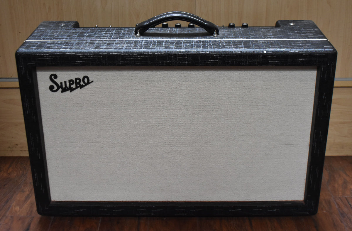 Front view of a black textured amplifier with a light gray grille cloth, black leather handle, and visible wear on the top edges.