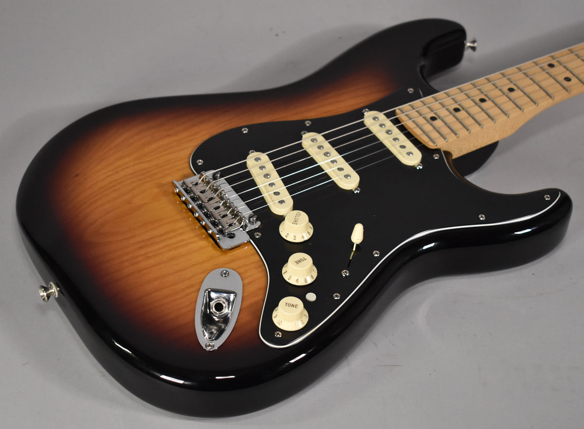 Angled view of a 3-tone sunburst Stratocaster with a black pickguard, three cream single-coil pickups, and cream control knobs.