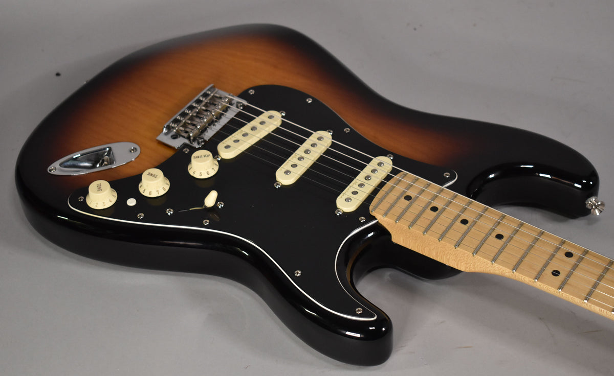 A glossy 3-tone sunburst electric guitar, angled from the lower bout, showing a black pickguard, three cream single-coil pickups, and a maple fretboard.