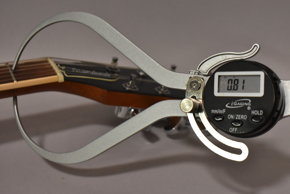 A digital caliper measures the guitar's nut width at 0.81, with the headstock and tuning pegs visible in the background.