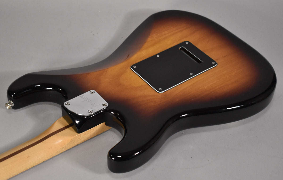 The guitar's glossy 3-tone sunburst back is angled, showing a black tremolo cavity cover and a chrome neck plate.