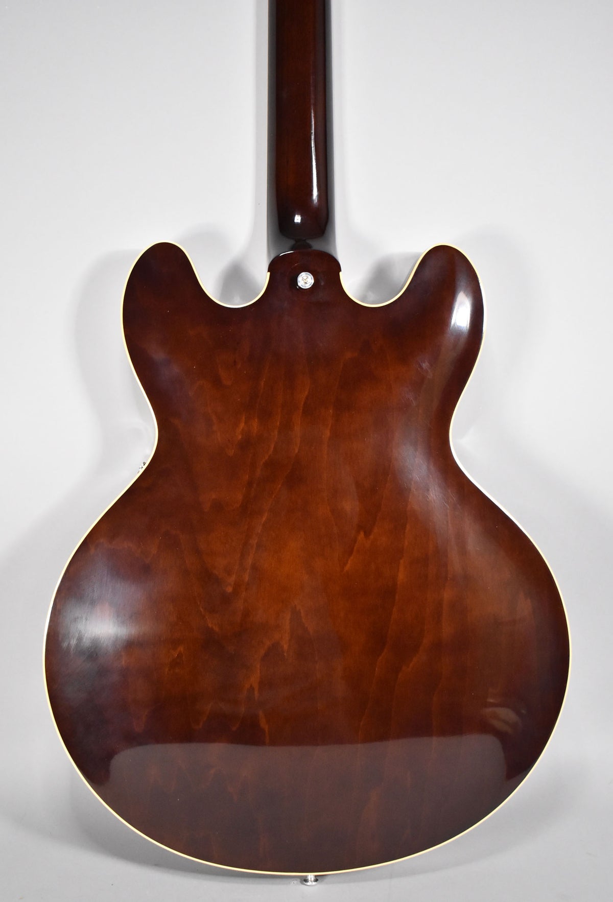 The guitar's back, a glossy dark walnut with visible wood grain, shows light checking and a small chip on the upper left horn.