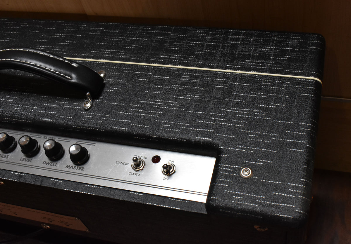Close-up of the amp's top, showing the black textured tolex with white piping, a leather handle, and the silver control panel with knobs and toggle switches.