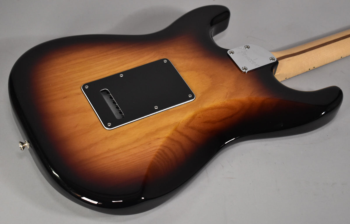 The guitar's glossy 3-tone sunburst back, with a black tremolo cavity cover and chrome neck plate, is angled from the lower left.