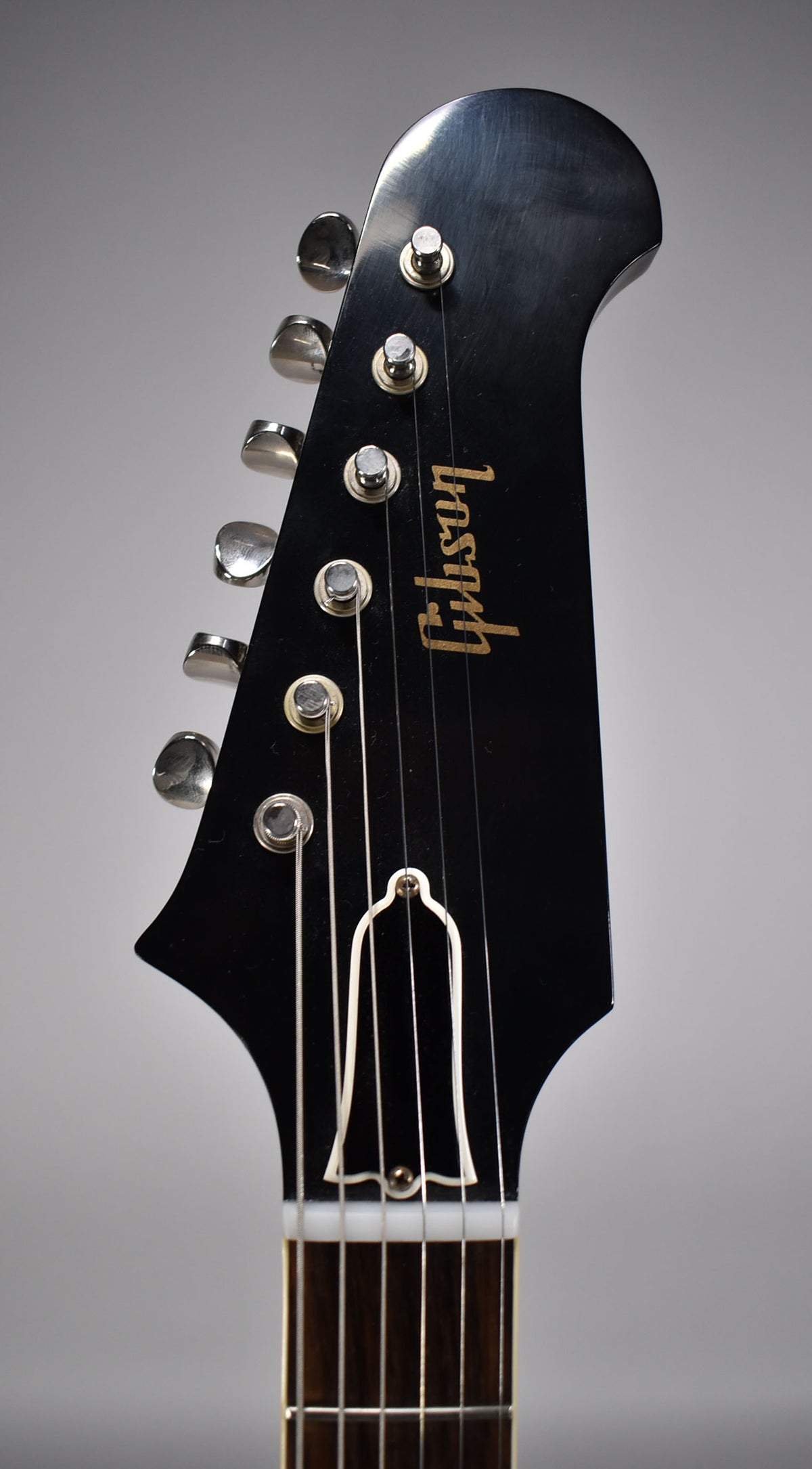 Close-up of the black headstock with gold logo, six chrome tuners, and white truss rod cover, showing light finish wear.