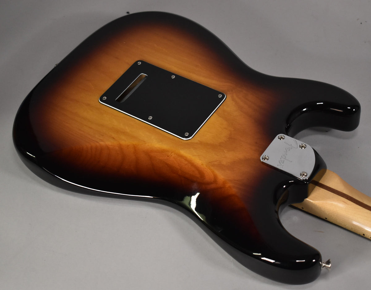 The guitar's glossy 3-tone sunburst back, with a black tremolo cover and chrome neck plate, is angled from the upper bout.