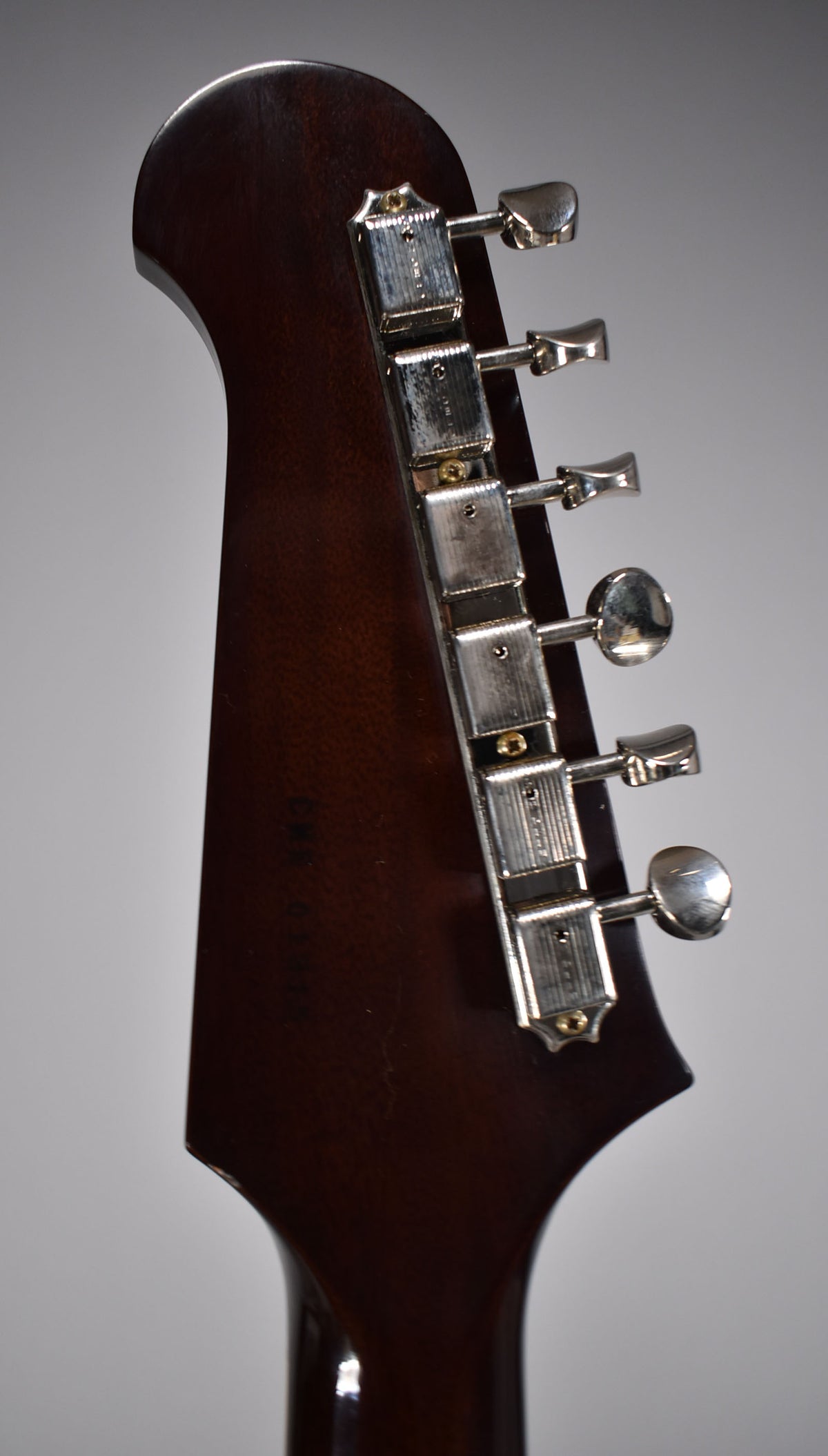 The dark walnut headstock, viewed from the back, shows six chrome tuners with light relicing and a faint serial number.