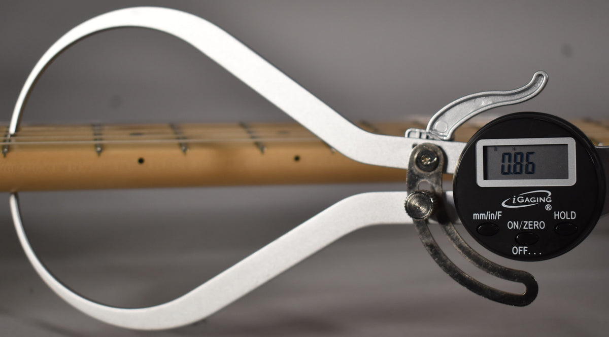 A digital string action gauge measures the height of the strings above the maple fretboard, displaying "0.86" on its screen.