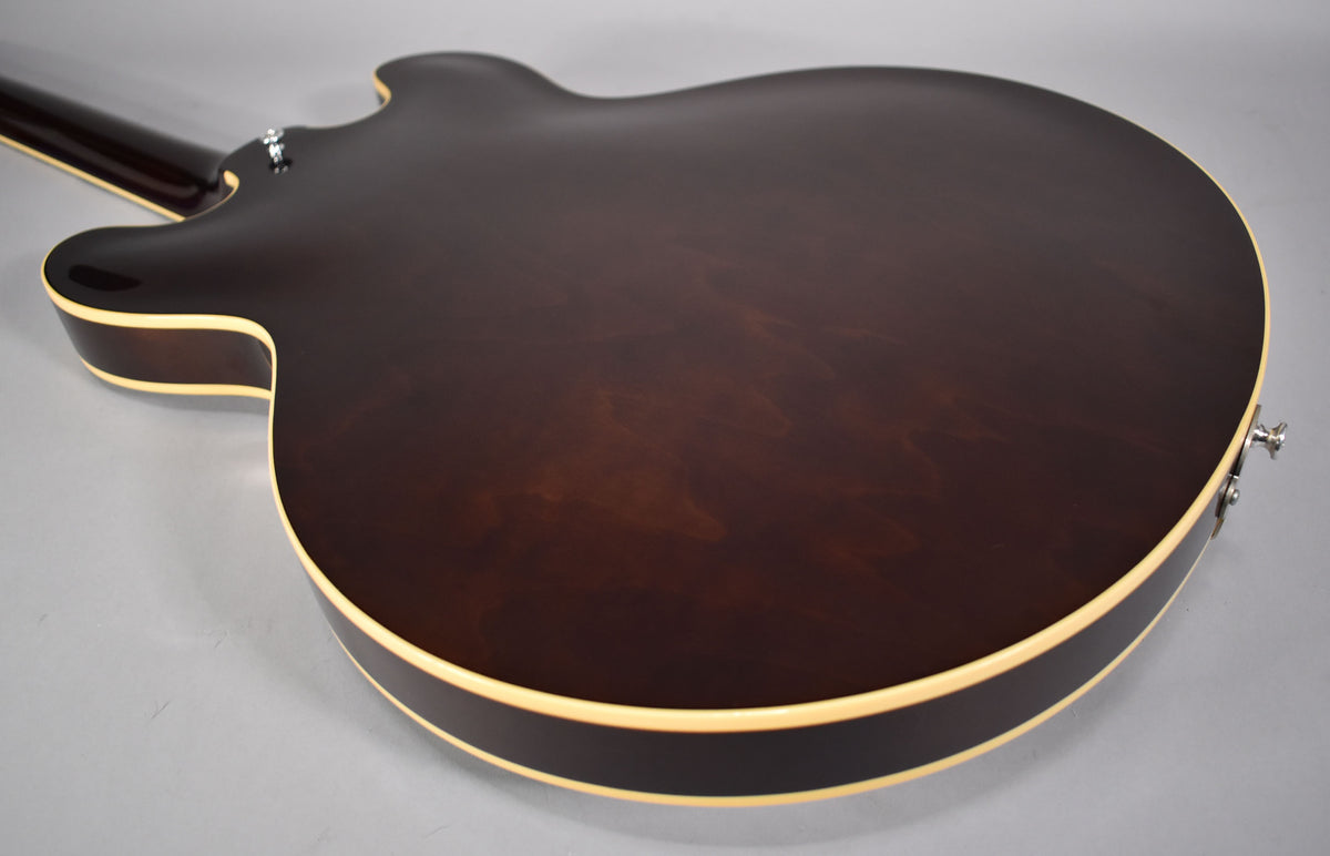 The back of a dark walnut semi-hollow electric guitar, showing its binding and a strap button, with subtle wood grain visible.
