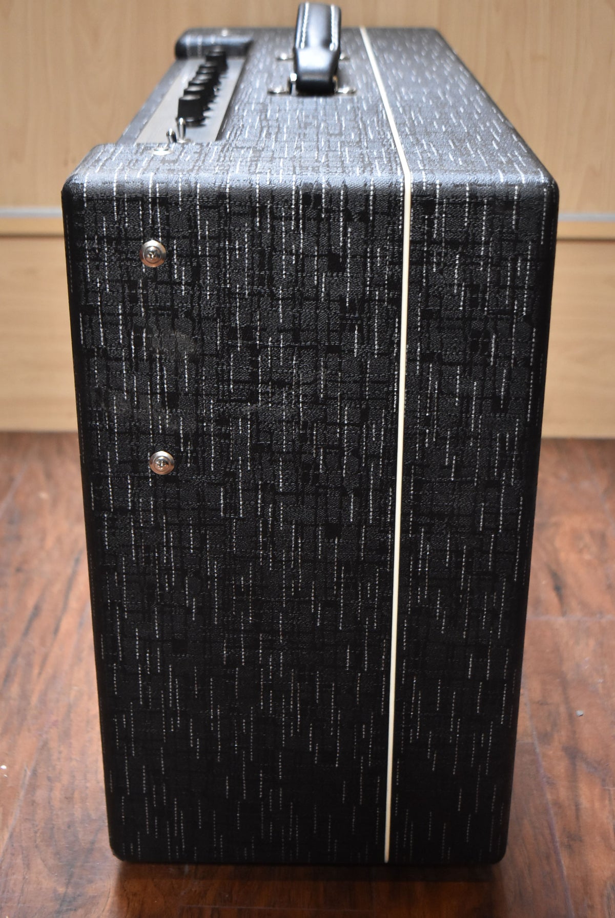 The amplifier's right side, covered in black textured tolex with white pinstripes and cream piping, is shown from a high angle.
