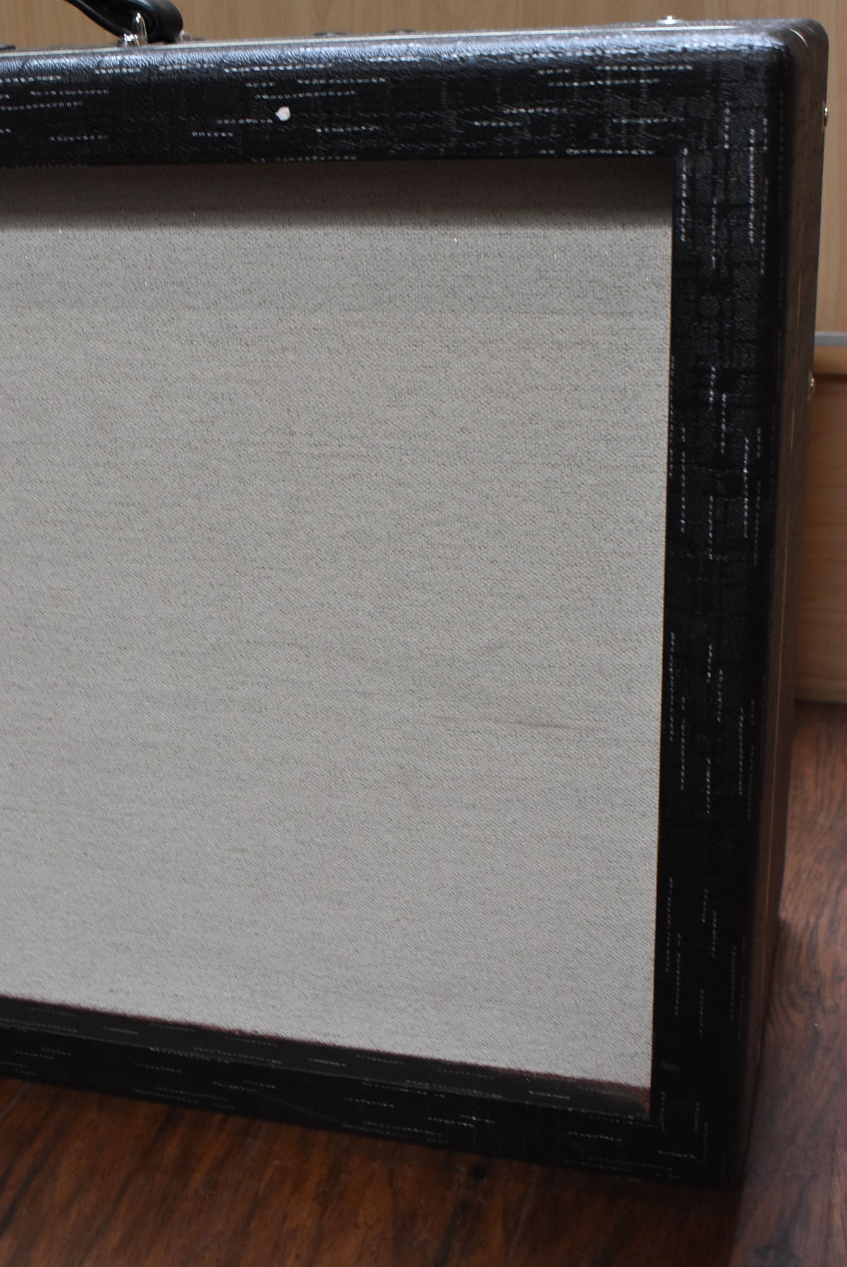 Close-up of the amp's upper right corner, showing the light gray grille cloth framed by black textured tolex with a white scuff.