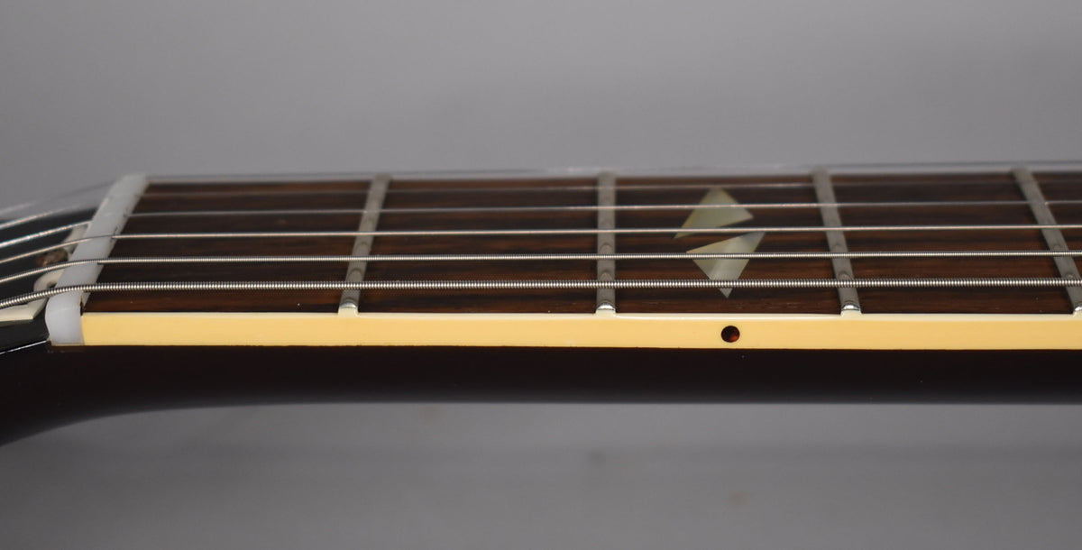 Close-up of the dark fretboard and strings, showing a diamond inlay, cream binding, and a small dot marker on the side.