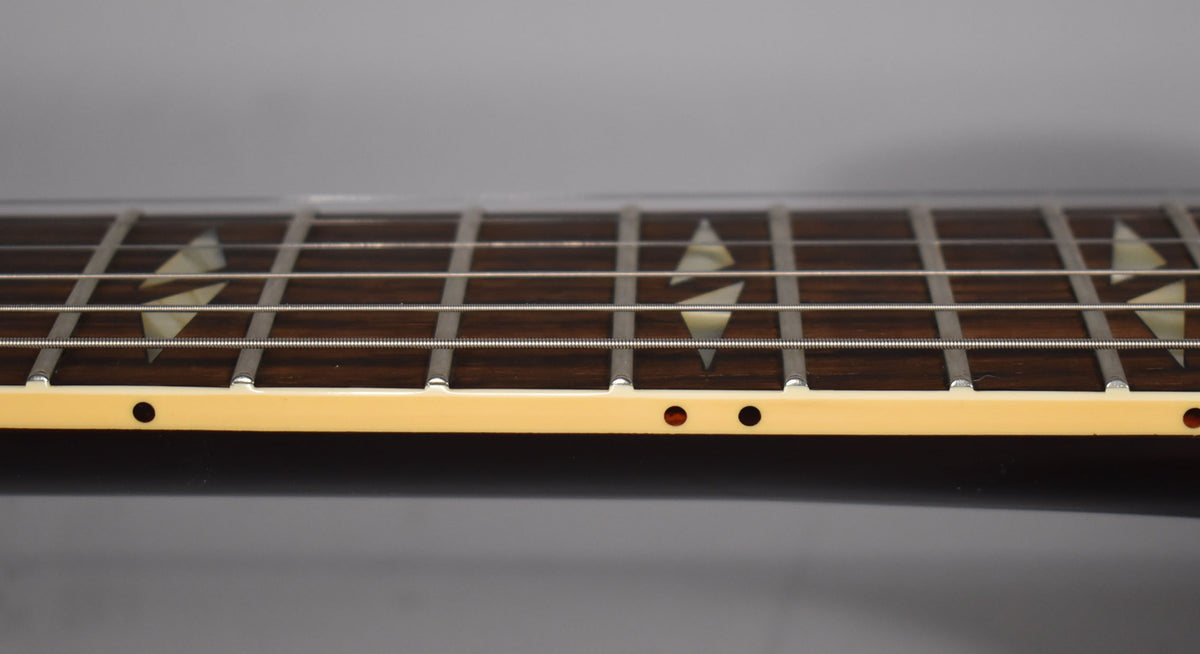 Close-up of the dark fretboard with trapezoid inlays, showing the cream binding with side dots and a hint of the walnut body.
